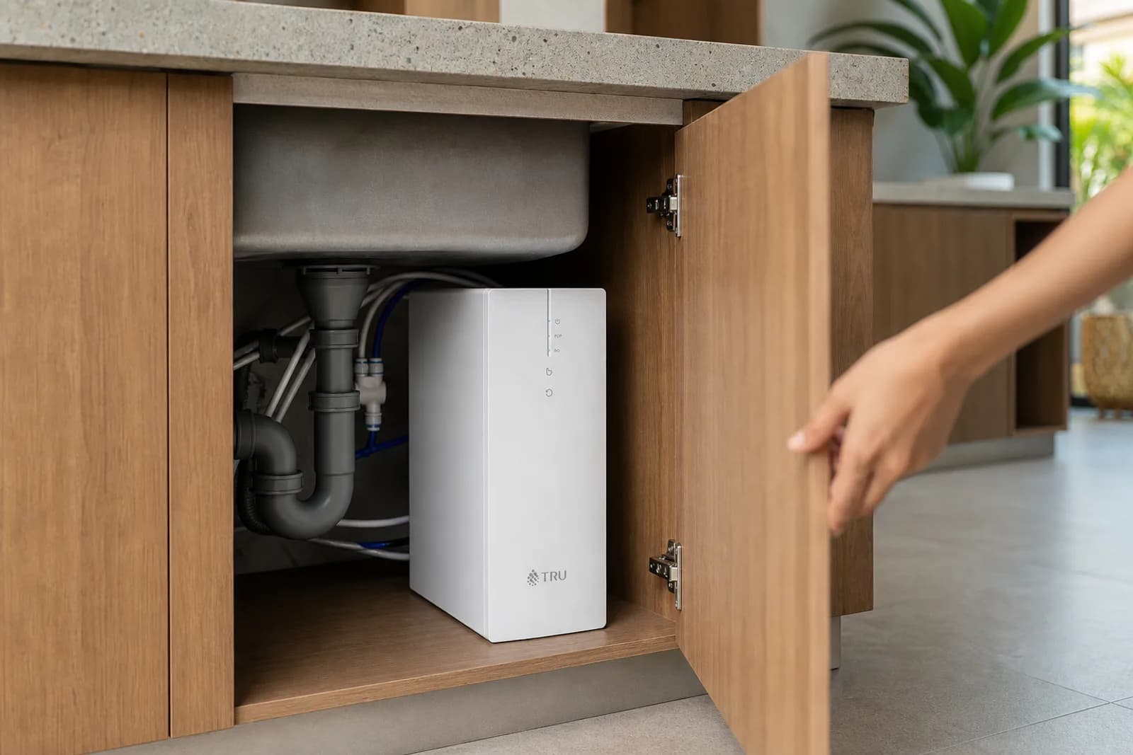 A hand opening an under-sink cabinet to reveal the compact slim purifier.