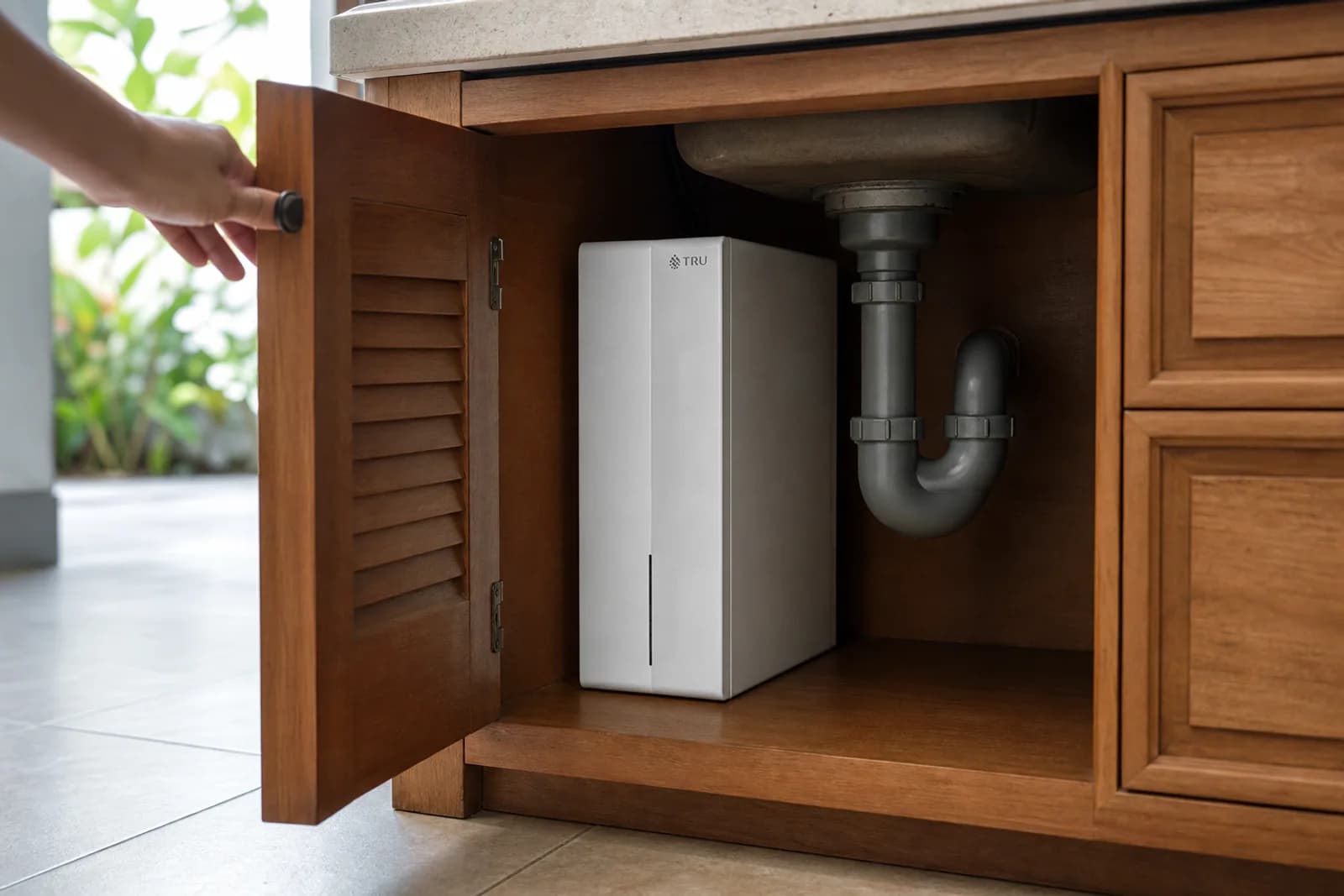 A hand opening an under-sink cabinet to reveal the compact purifier unit.